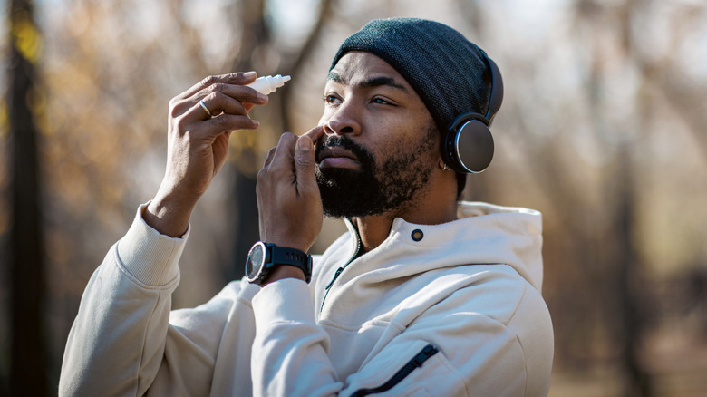 young man outside putting eye drops into his eyes