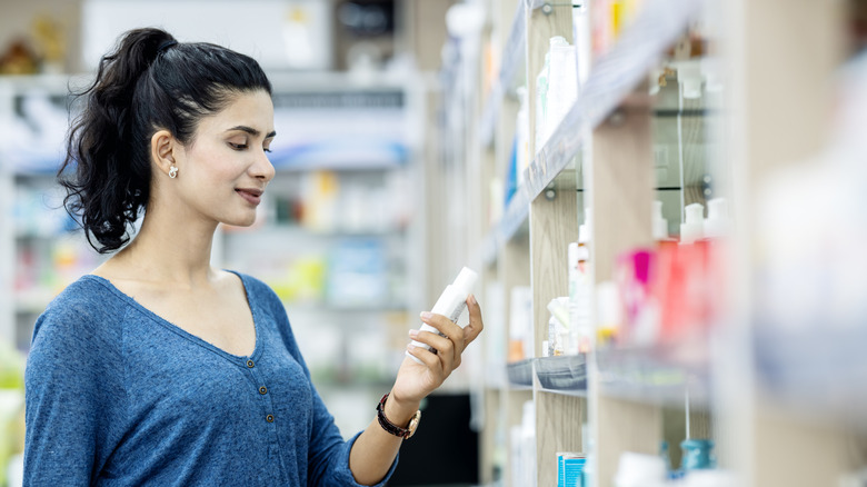 A woman looking at the label of a skincare product at a pharmacy