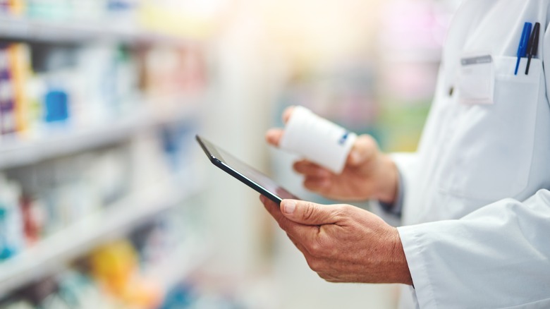 technician in pharmacy looking at pill bottle and phone