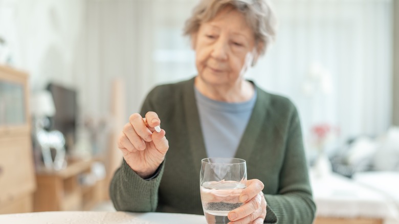 mature woman holding pill and glass of water