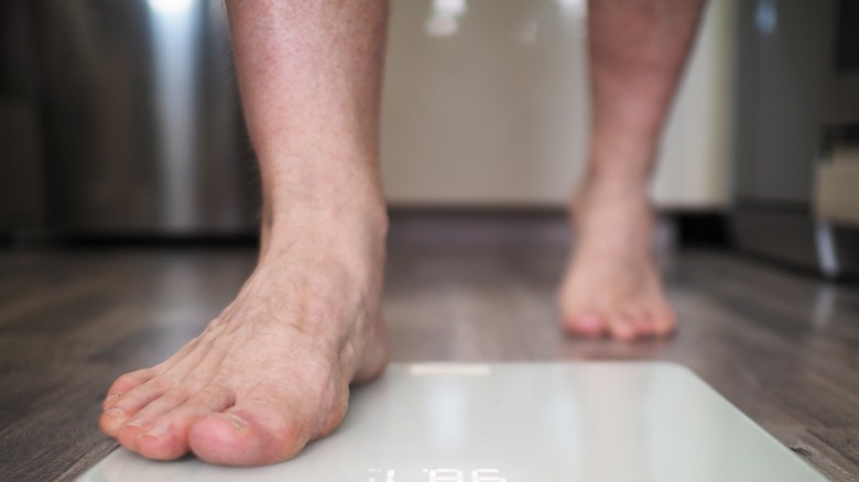 man walking on scale to weigh himself at home