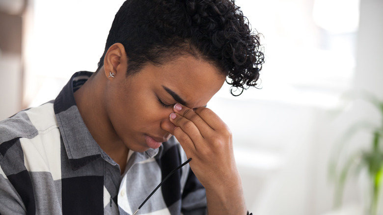 Person with closed eyes holding the bridge of their nose in discomfort