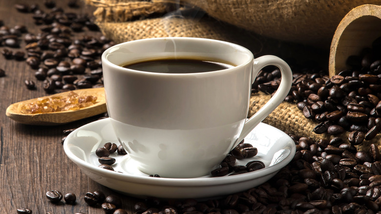 Steaming cup of coffee surrounded by coffee beans