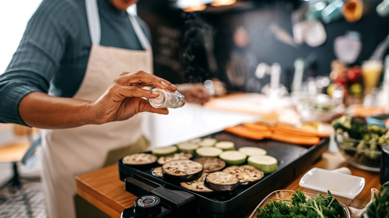 A woman adding salt to sliced eggplant on a griddle
