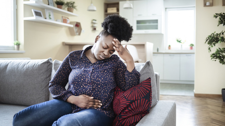 woman sitting on sofa holding stomach