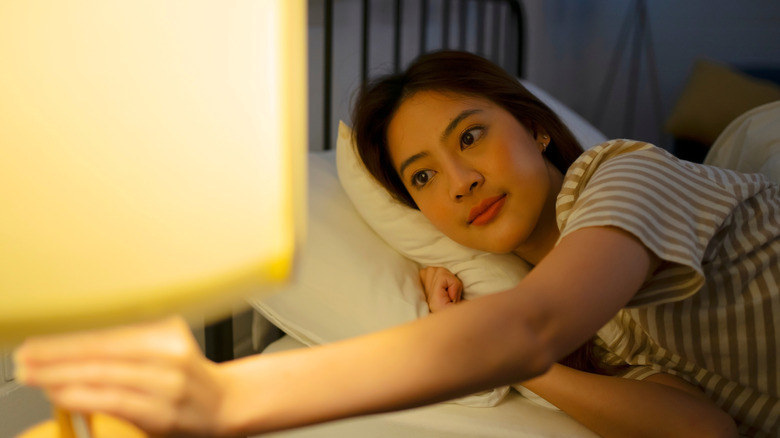 young woman turning off lamp next to bed