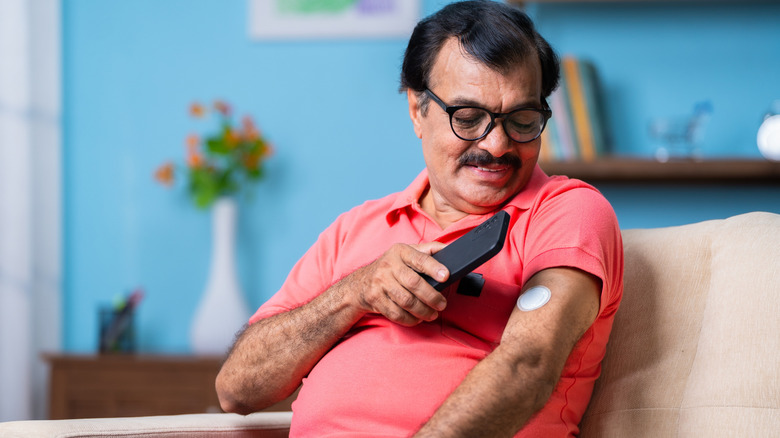 man sitting on sofa checking his glucose levels