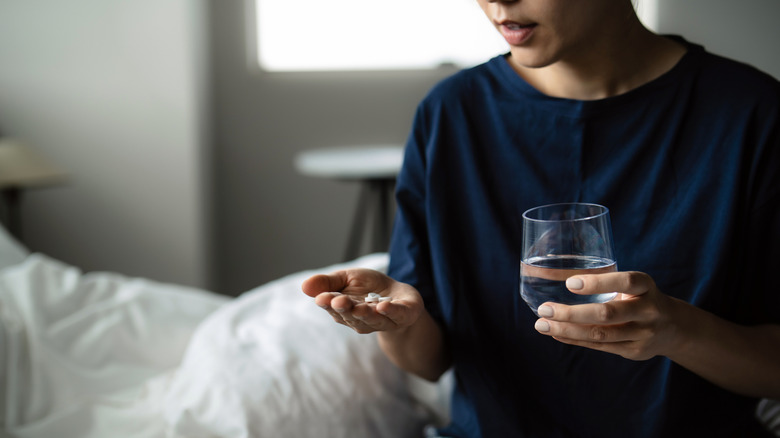 A woman's hand holding a glass of water and a medication pill