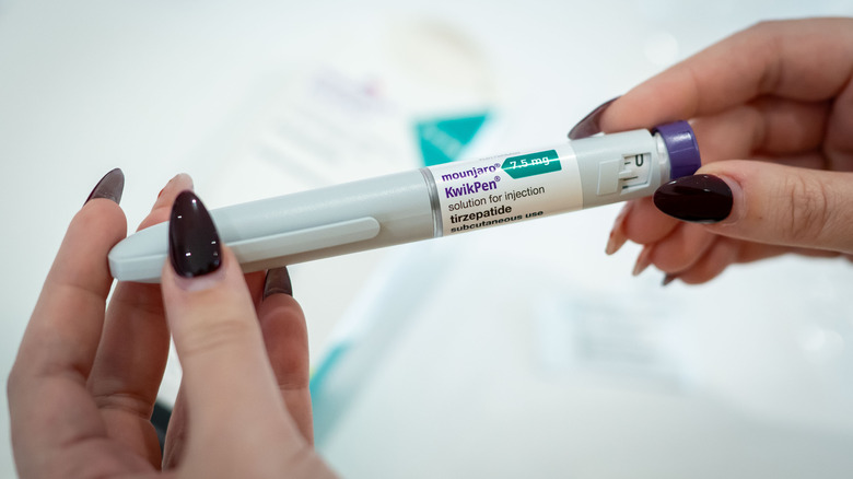 Two hands with painted nails holding the Mounjaro pen.