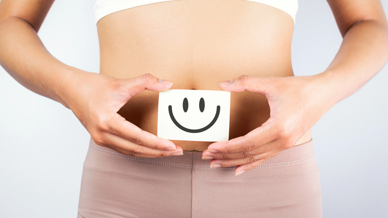 A woman holds a smiley face by her stomach