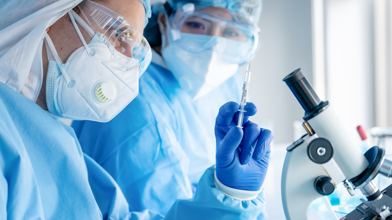 Researchers wearing protective gear holding syringe 