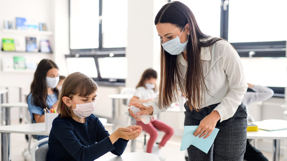 Teacher giving student hand sanitizer in classroom