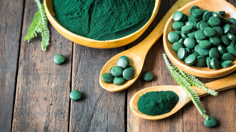 spirulina powder and tablets in bowls on a wooden table 