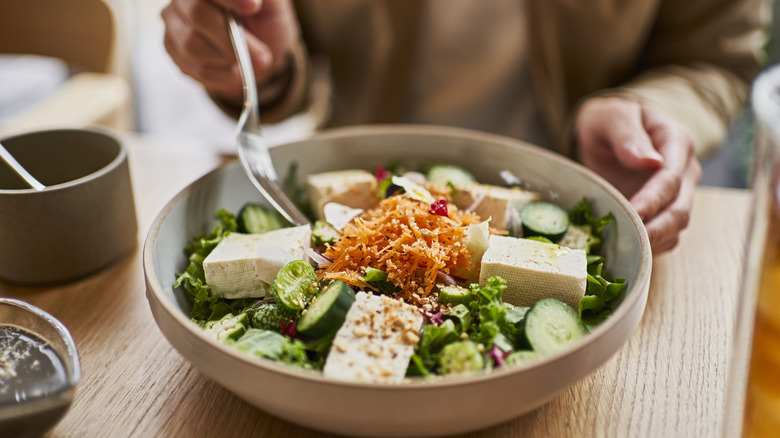 A vegan spinach salad with tofu, cucumbers, and carrots