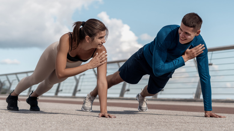A man and a woman tapping their shoulders while in a straight-arm plank hold