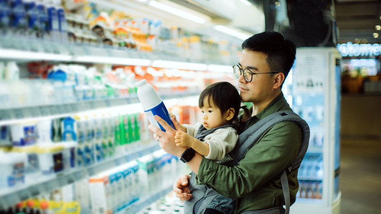 man carrying child and looking at bottle of coconut milk