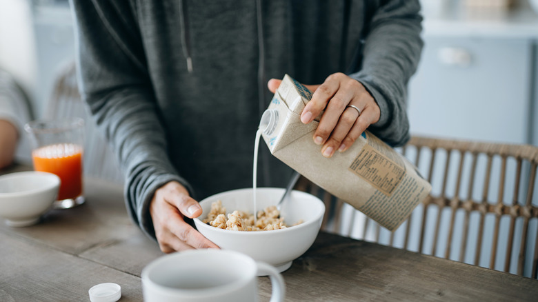 person pouring soymilk on cereal
