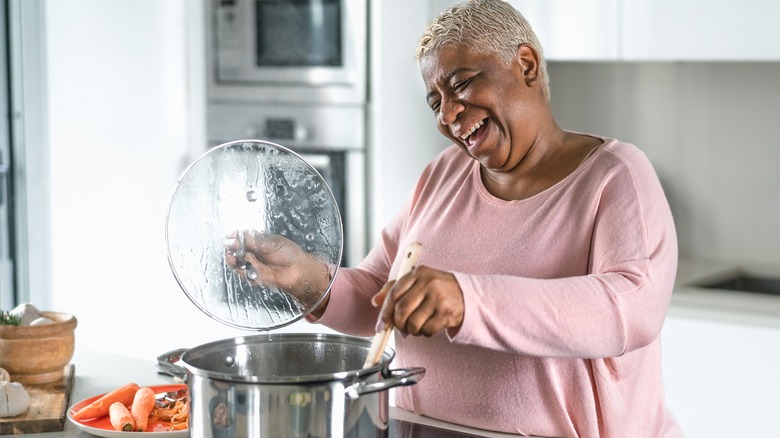 happy older woman stirring large pot on the stove