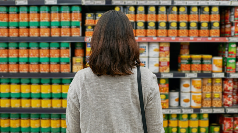 A woman looking at canned beans in a store aisle