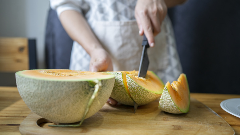 A woman's hands cutting into cantaloupe on a wood cutting board
