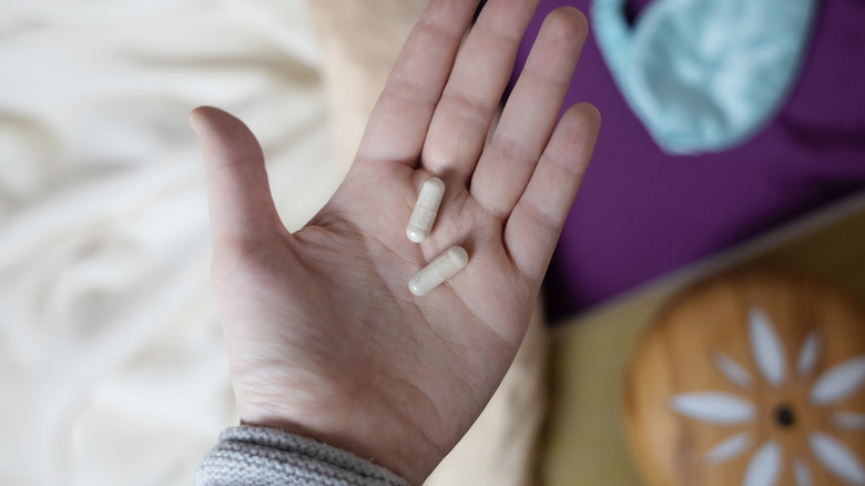 A woman's hand holding two melatonin capsules