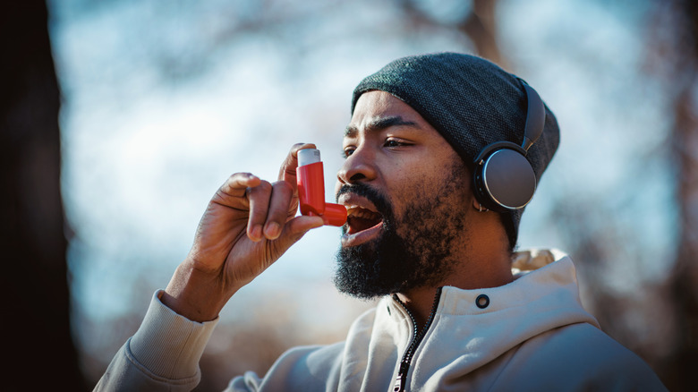 A man using an asthma inhaler while exercising outdoors