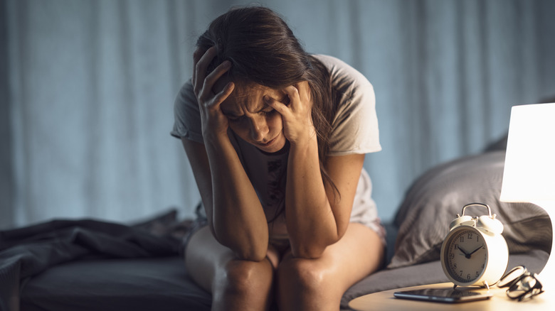 A woman sitting up on the side of her bed unable to sleep