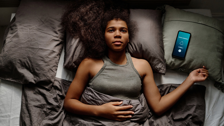 A woman lying awake on her bed with her phone nearby
