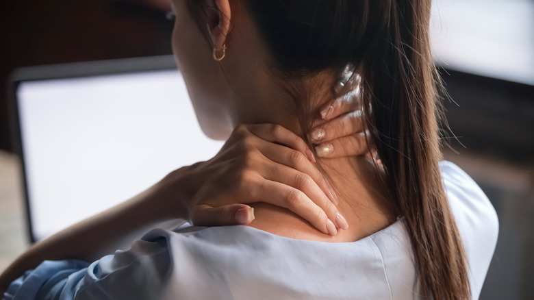 A woman rubbing her neck while seated at a computer