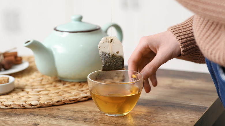 woman removing tea bag from cup of green tea