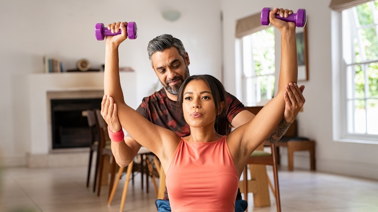 trainer helping a client with dumbbell overhead press