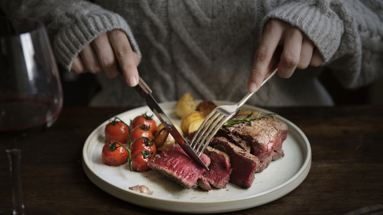 hands cutting into a steak