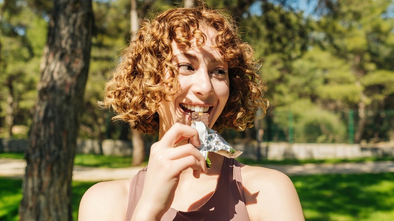 woman eating protein bar in park