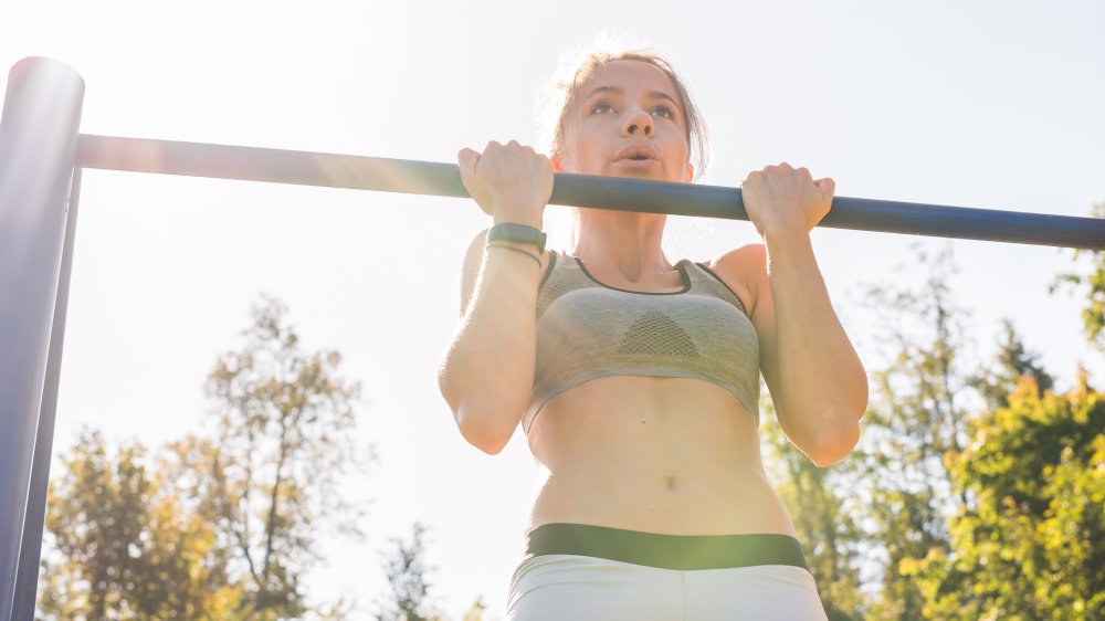 Woman does chin-ups outdoors on playground equipment