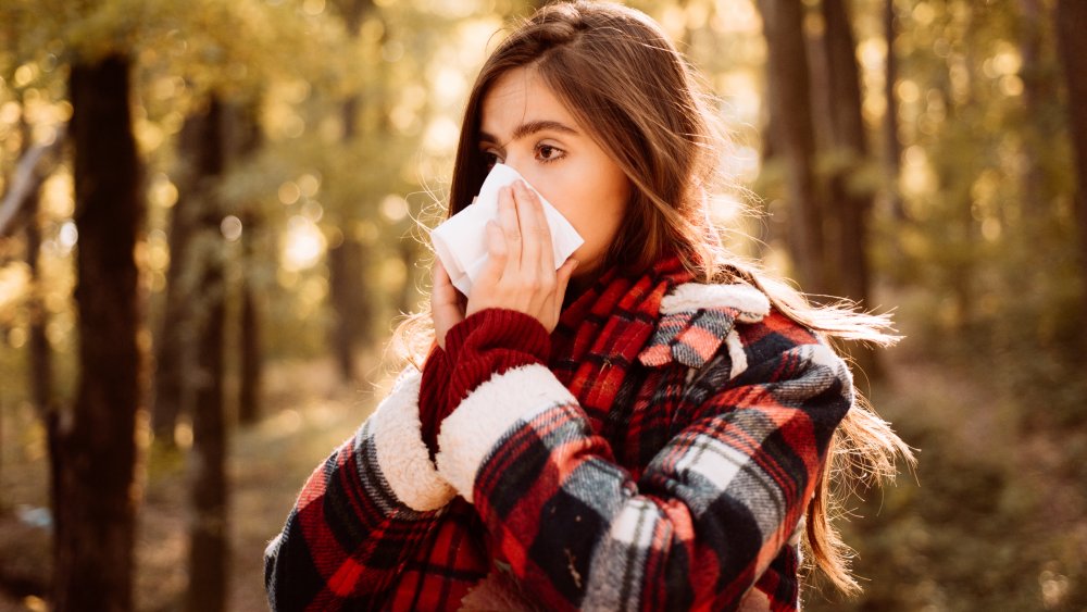 woman sneezing outside in the fall