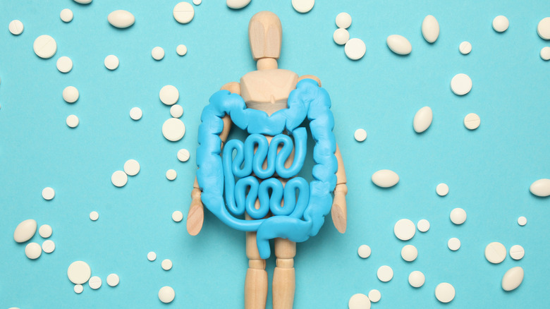 Wooden figure with blue intestines surrounded by probiotic pills on blue background