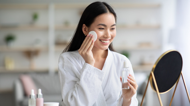 young asian woman hold cotton pads to cheeks