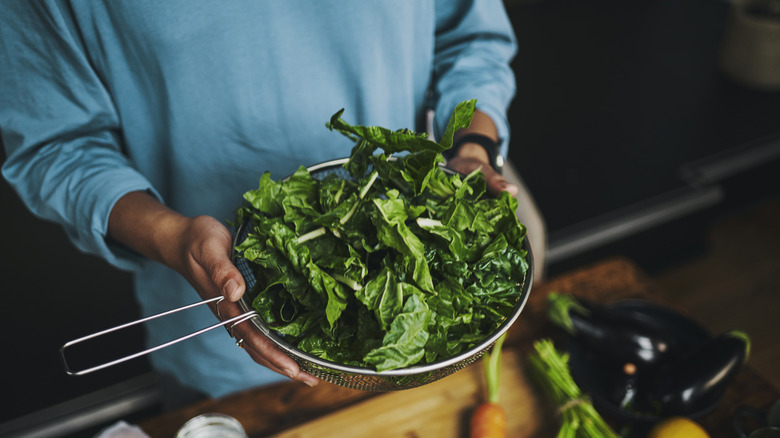 person holding colander of manganese-rich leafy greens