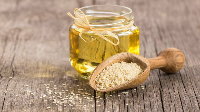 glass jar of sesame oil and a scoop of raw sesame seeds in front 