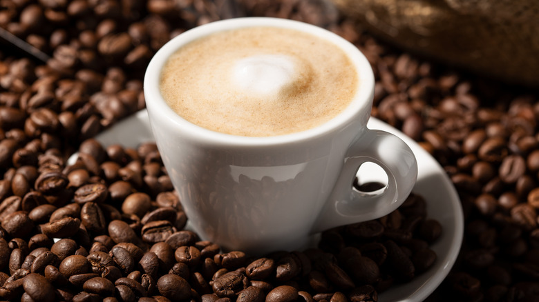 Close up of cup of coffee with milk on bed of coffee beans