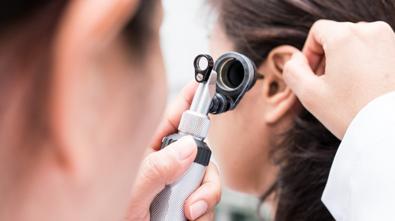 Doctor looking in woman's ear with an otoscope 