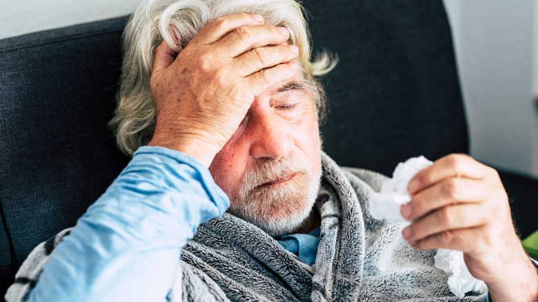 An ill man with his hand a tissue in one hand and his other hand on his brow