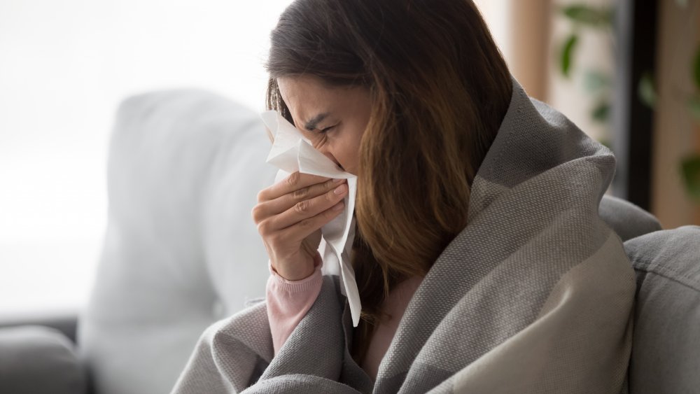 Ill woman in a blanket with tissues on a sofa