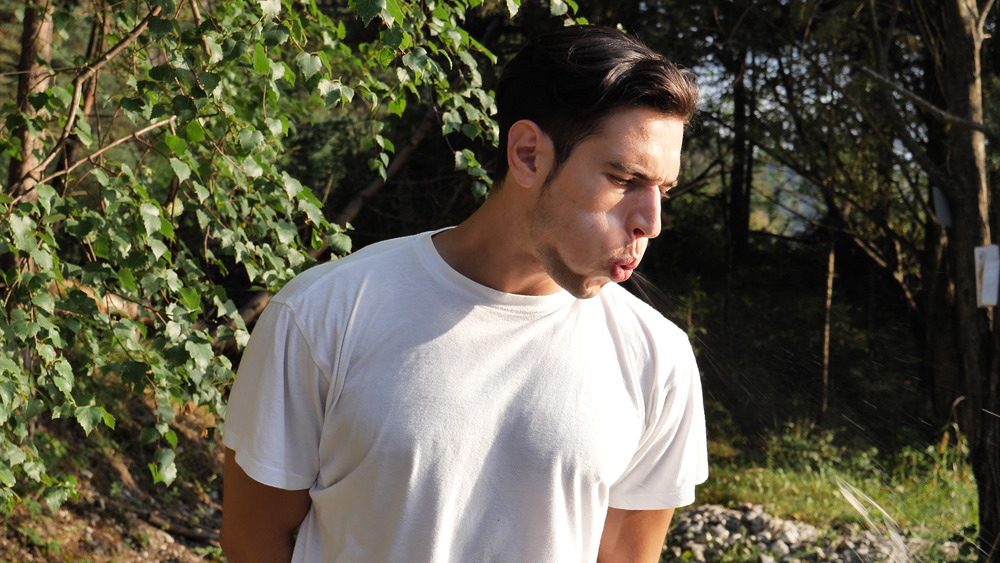 Young man in a white T-shirt spitting outside 
