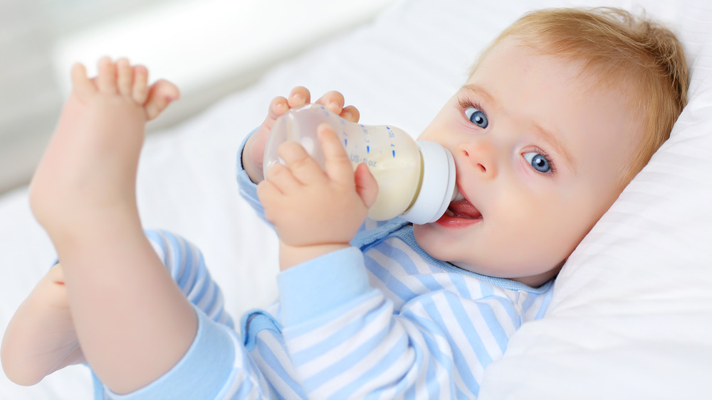 Baby lying on back drinking milk from bottle