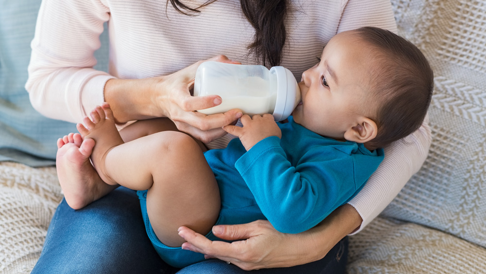 Baby sitting in mother's lap drinking milk from a bottle