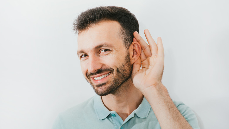 A smiling man cupping his ear