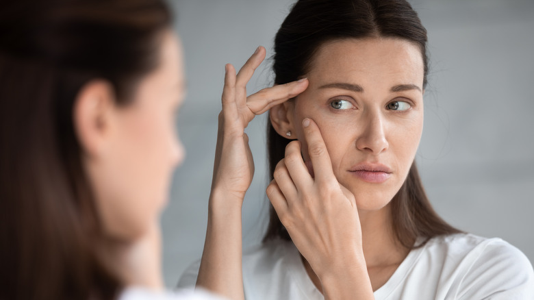 A woman looks for wrinkles in the mirror