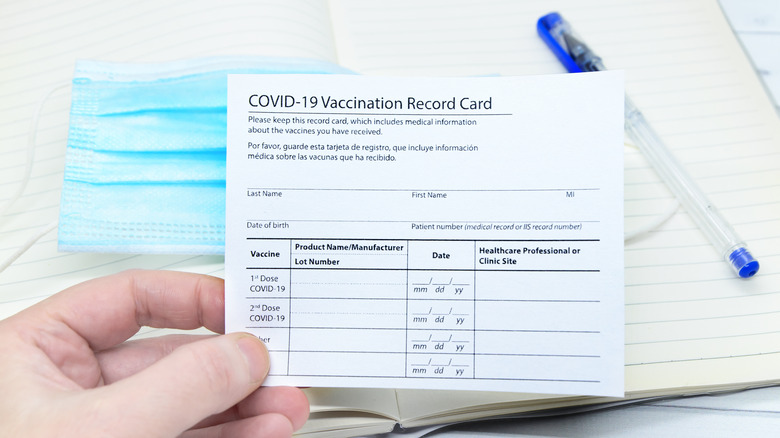 Womans hand holds coronavirus vaccination record card on background blue medical mask.