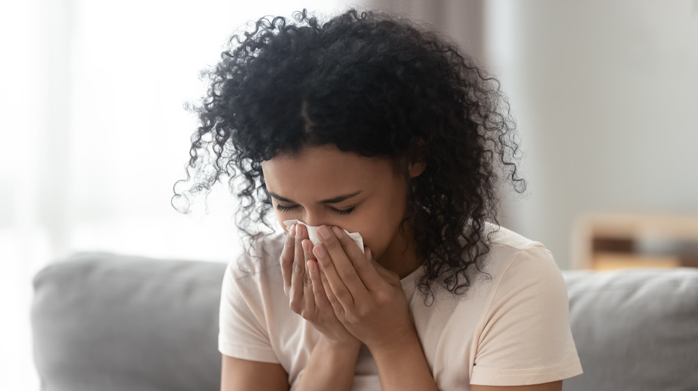 Woman sitting on the couch and blowing her nose